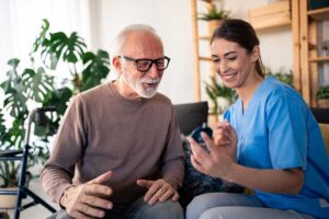 A caregiver assists an older adult with daily activities in a comfortable home living room.